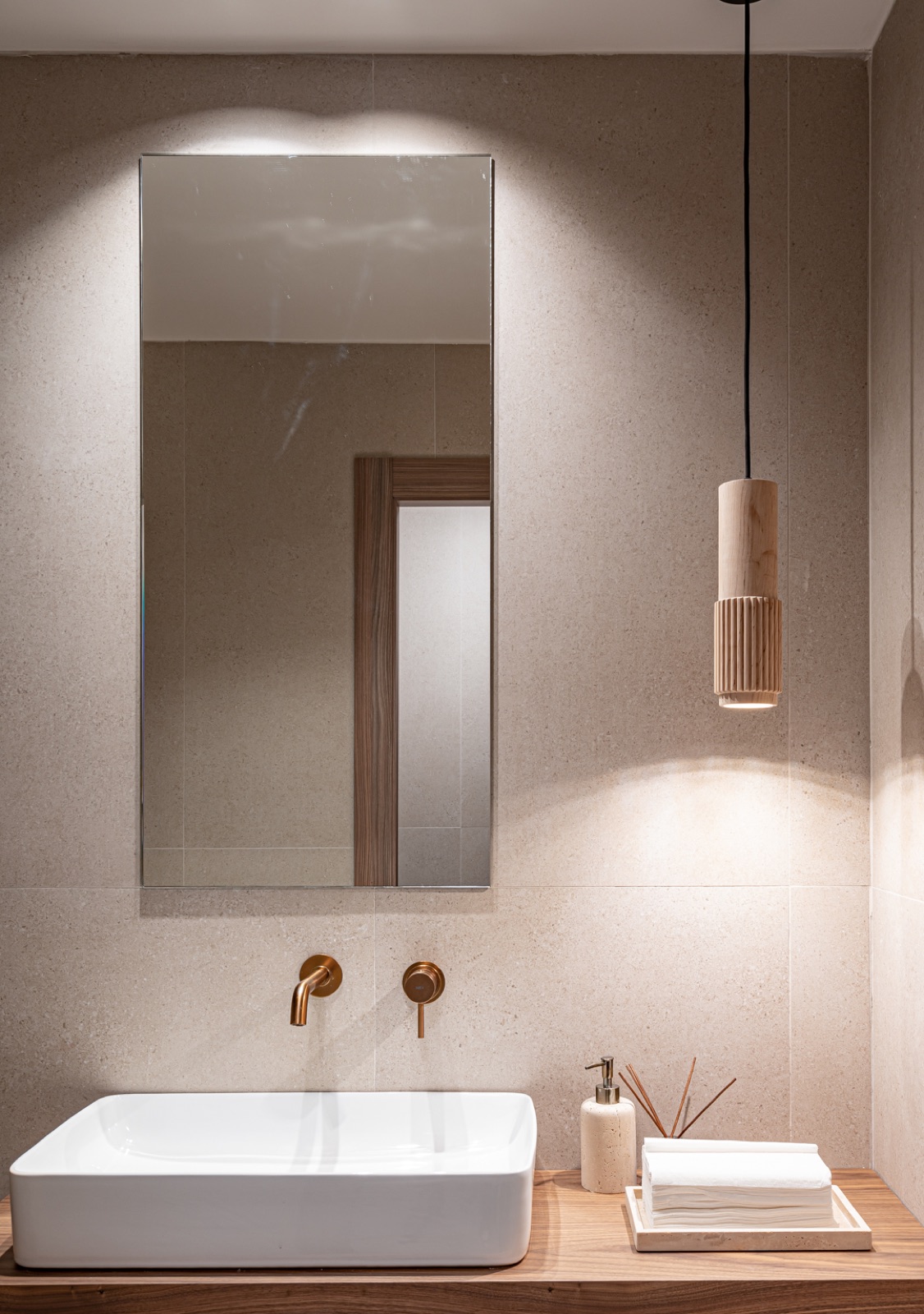 Lavabo sobre encimera de madera con grifería dorada empotrada y lámpara colgante cerámica