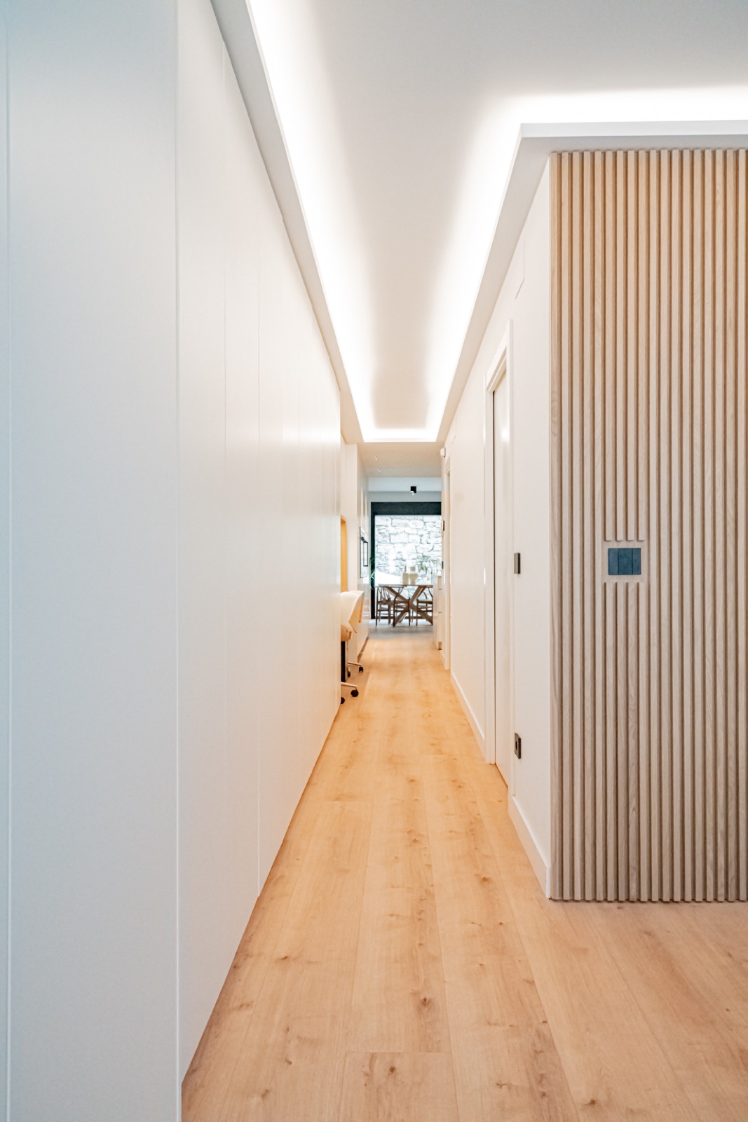 Pasillo con iluminación LED perimetral y pared de listones de madera natural