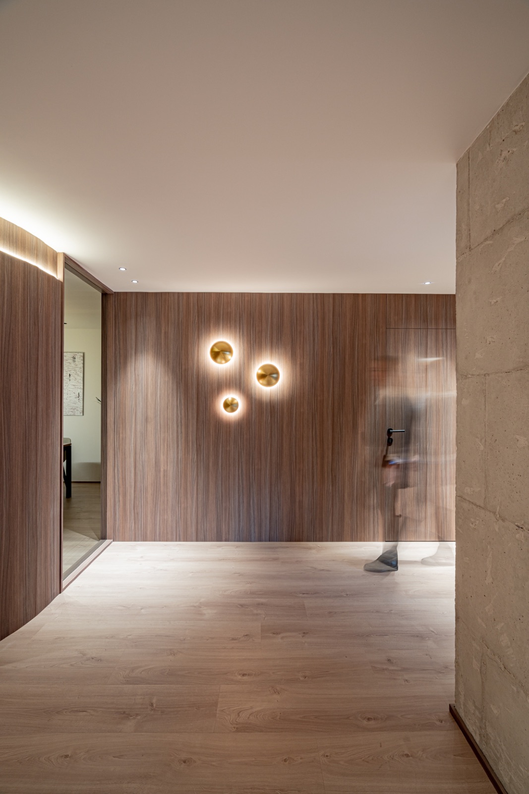 Vestíbulo con revestimiento de madera oscura, apliques dorados y muro de piedra